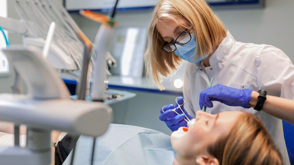 Zahnärztin mit Mundschutz arbeitet über einen Patienten gebeugt.