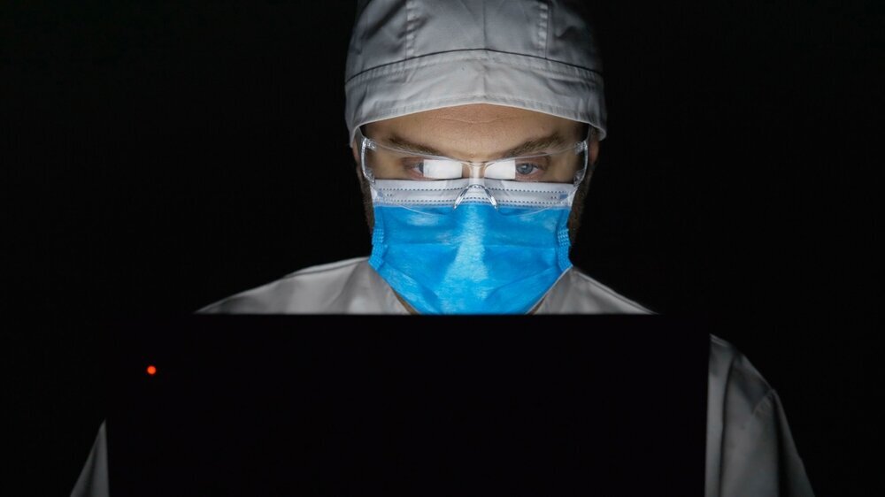 Portrait of man doctor with mask look at laptop late night Porträt eines Arztes mit Maske, der spät in der Nacht auf den Laptop schaut