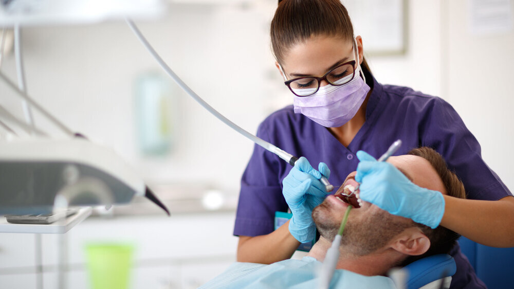 Junge Zahnärztin beim Bohren eines Zahns für einen Patienten in einer Zahnklinik Junge Zahnärztin beim Bohren eines Zahns für einen Patienten in einer Zahnklinik
