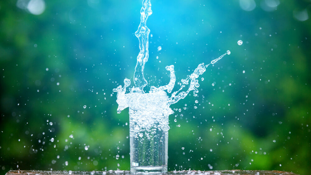 Wasser spritzt aus einem Glas vor grünem Hintergrund