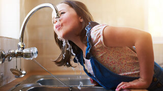 A kittle girl drinking water directly from the kitchen tap at home.