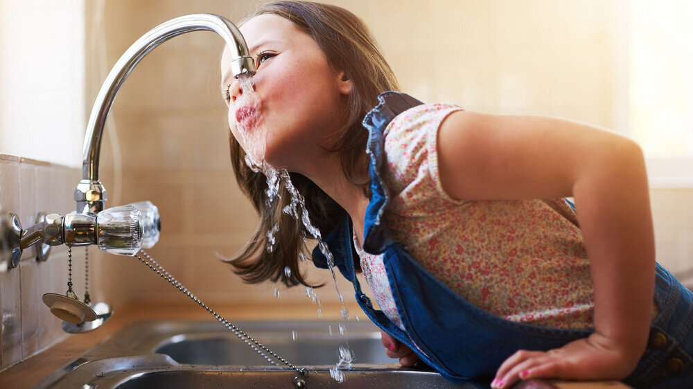 A kittle girl drinking water directly from the kitchen tap at home.