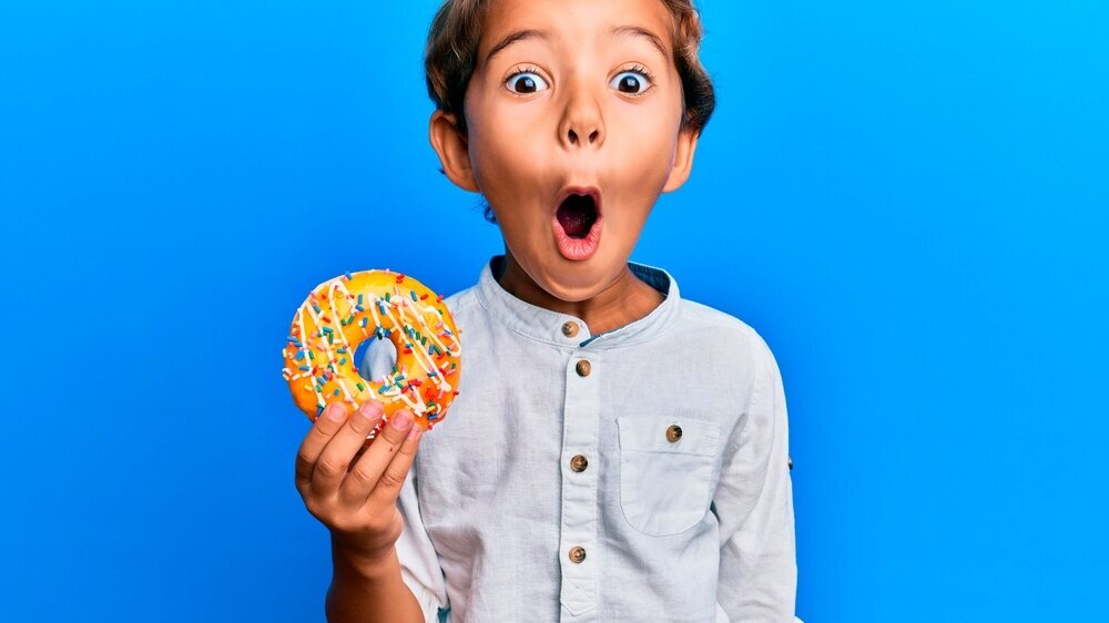 Adorable latin kid holding donut scared and amazed with open mouth for surprise, disbelief face Junge Donut