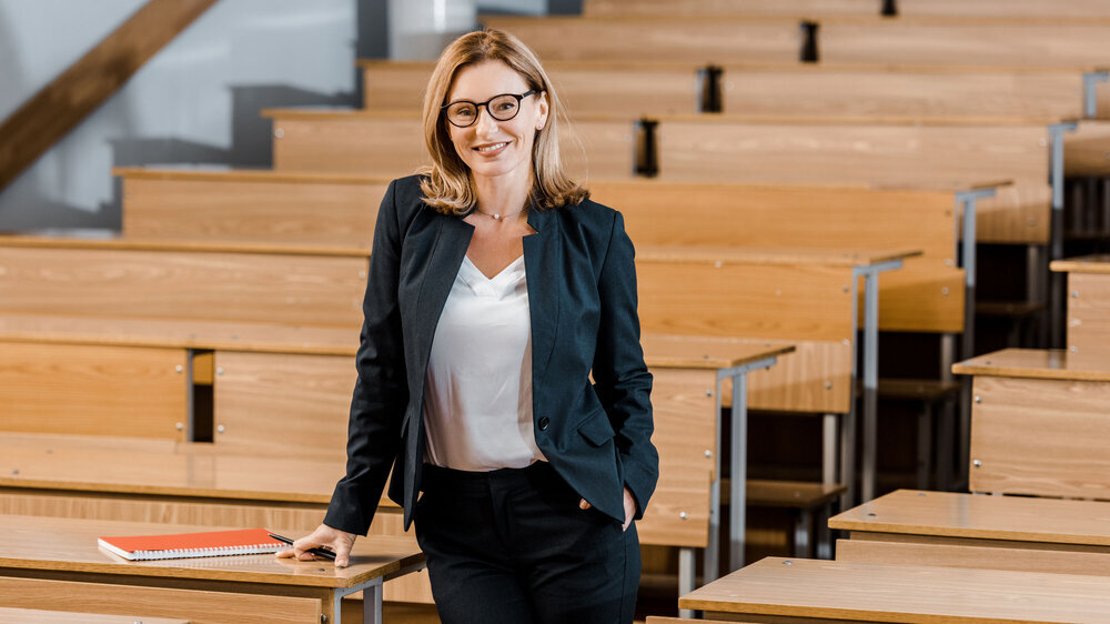 Universitätsprofessorin lächelt und schaut in die Kamera im Klassenzimmer. Universitätsprofessorin lächelt und schaut in die Kamera im Klassenzimmer.