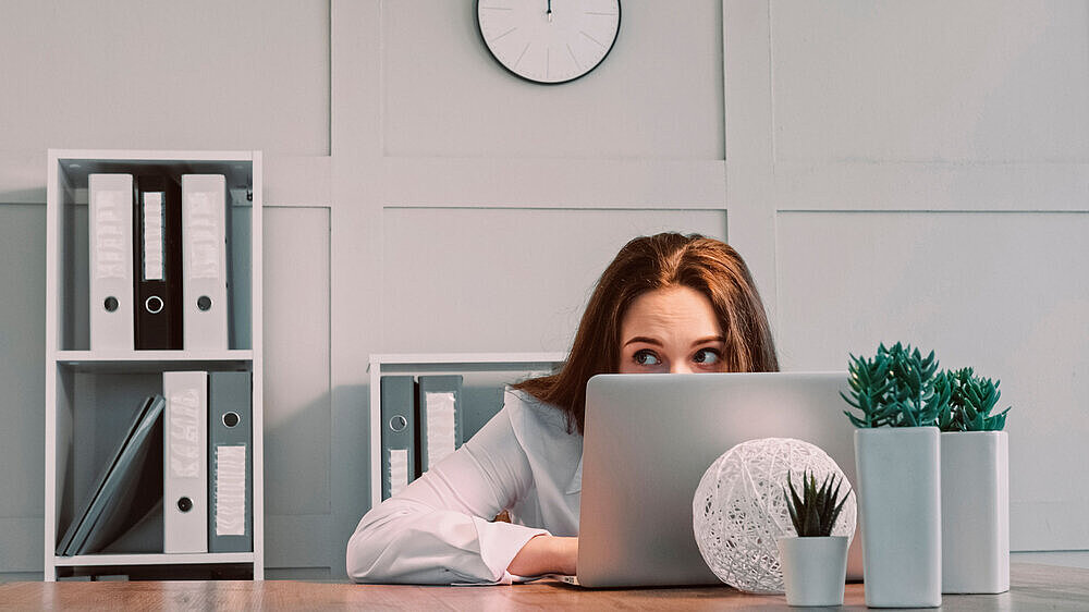 Eine junge Frau versteckt sich hinter ihrem Laptop, um bei der Arbeit nicht konfrontiert zu werden. Eine junge Frau versteckt sich hinter ihrem Laptop, um bei der Arbeit nicht konfrontiert zu werden.