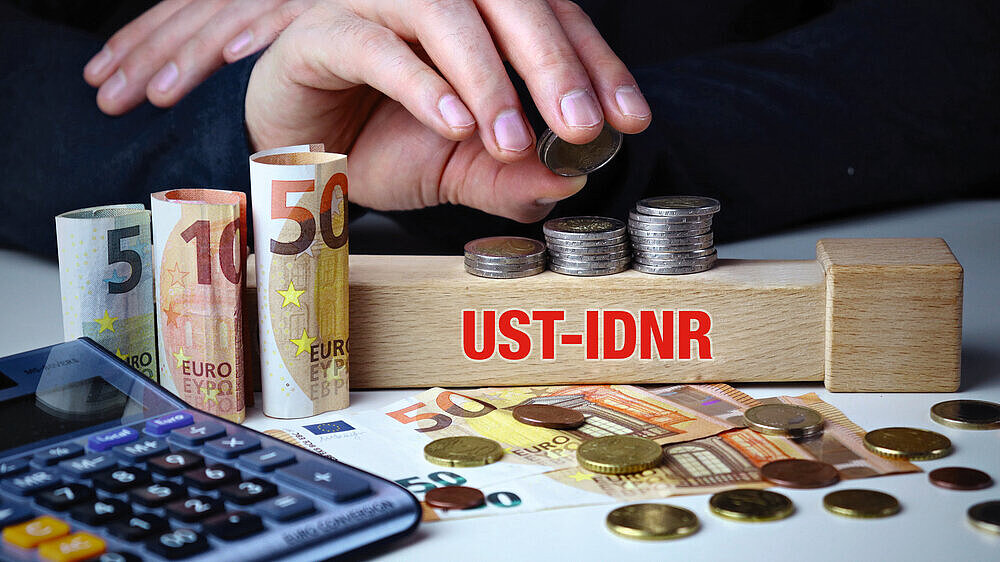USt-IdNr. Männliche Hand stapelt Geld-Turm (Euro). Begriff an Baustein. Münzen, Scheine & Taschenrechner. Konzept für Business, Finanzen, Statistik