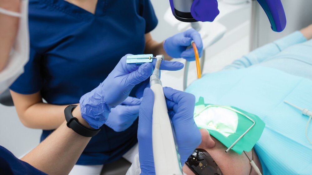Close-up picture of dental instruments: drill and needle for root canal treatment and pulpitis in hand at the dentist in a blue glove Macro photo of dental instruments: drill and needle for treating root canals and pulpitis in a dentist hand in a blue glove. The doctor measures the length of the needle with a special ruler