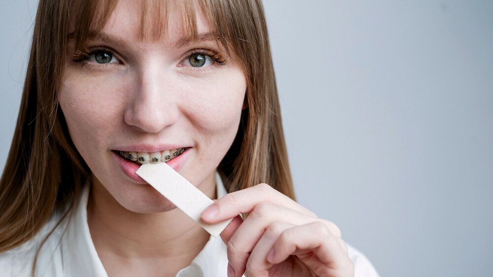 Young woman with metal braces on her teeth is chewing gum. The girl is eating gummy candy.