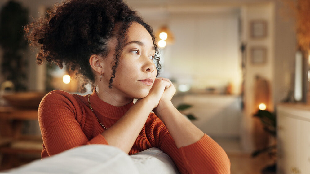Depression, lonely and sad with face of woman on sofa in living room of home for contemplation. Bored, heartbreak and thinking with unhappy African person in apartment for breakup or separation.