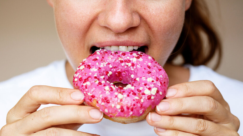 Close-up of a woman eating a donut with pink glaze. Close-up of a woman eating a donut with pink glaze.