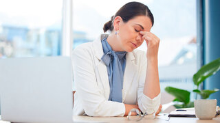 Stress, burnout and healthcare with a doctor woman suffering from a headache while working on a laptop in a hospital. Mental health, medicine and medical with a female health professional in a clinic.
