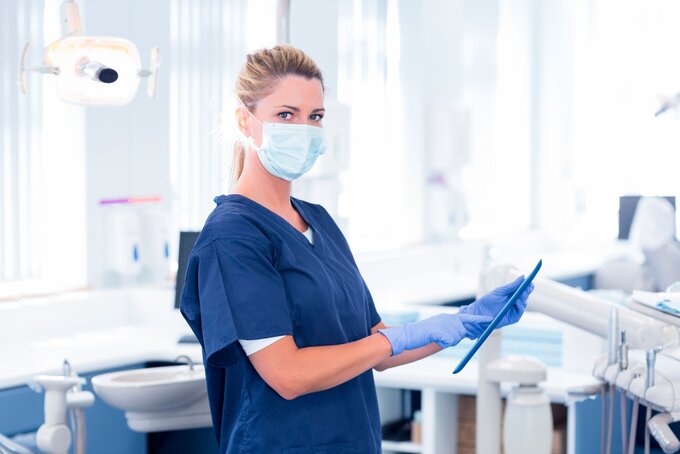 Zahnmedizinische Fachangestellte ZFA im Behandlungszimmer mit Tablet in der Hand.