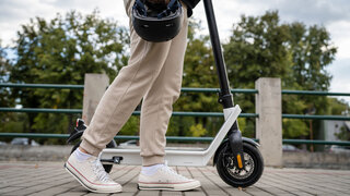 Feet of unknown man standing by or driving electric kick scooter e-scooter on the pavement in day eco friendly modern transport