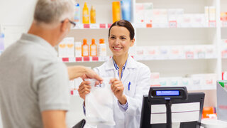 medicine, pharmaceutics, health care and people concept - female apothecary giving senior male customer his purchase in bag at drugstore