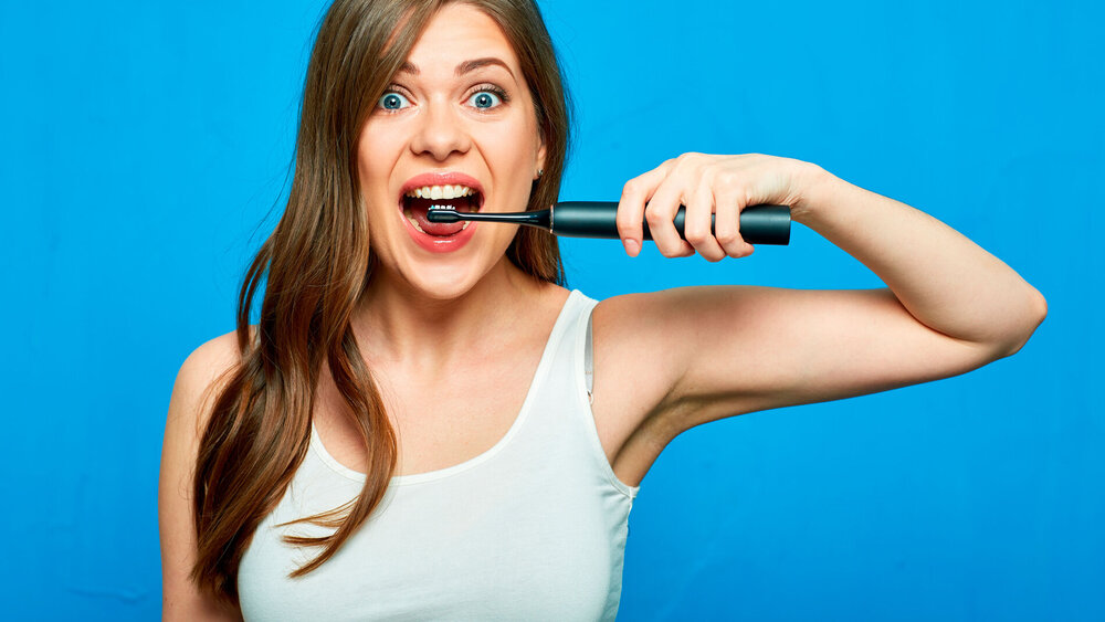 Junge Frau hält elektrische Zahnbürste vor den geöffneten Mund.