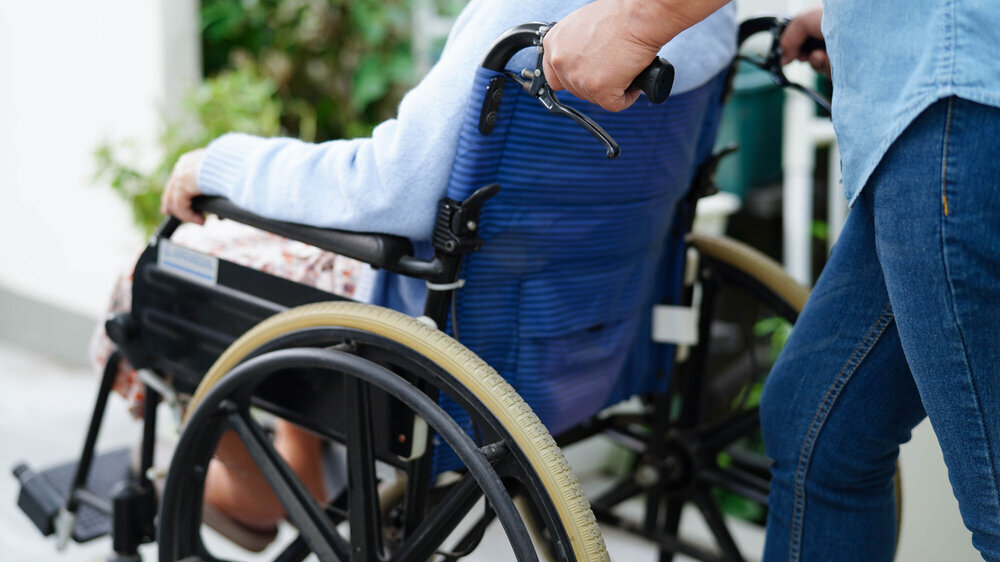 Pflegekraft hilft älterer Frau mit Behinderung in der Praxis, die im Rollstuhl sitzt.