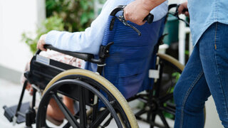 Pflegekraft hilft älterer Frau mit Behinderung in der Praxis, die im Rollstuhl sitzt.