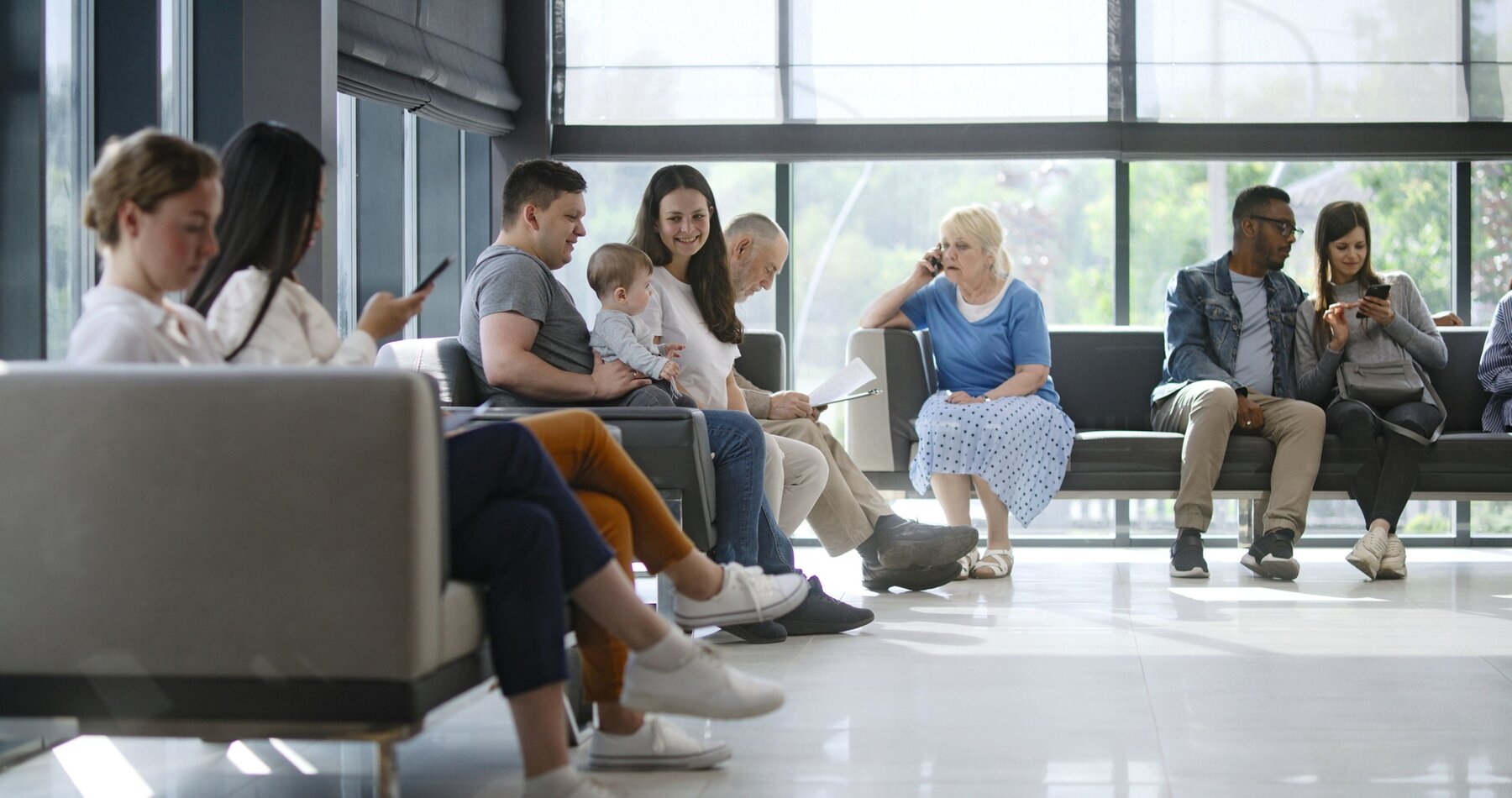 Verschiedene Menschen sitzen im Wartebereich einer Arztpraxis