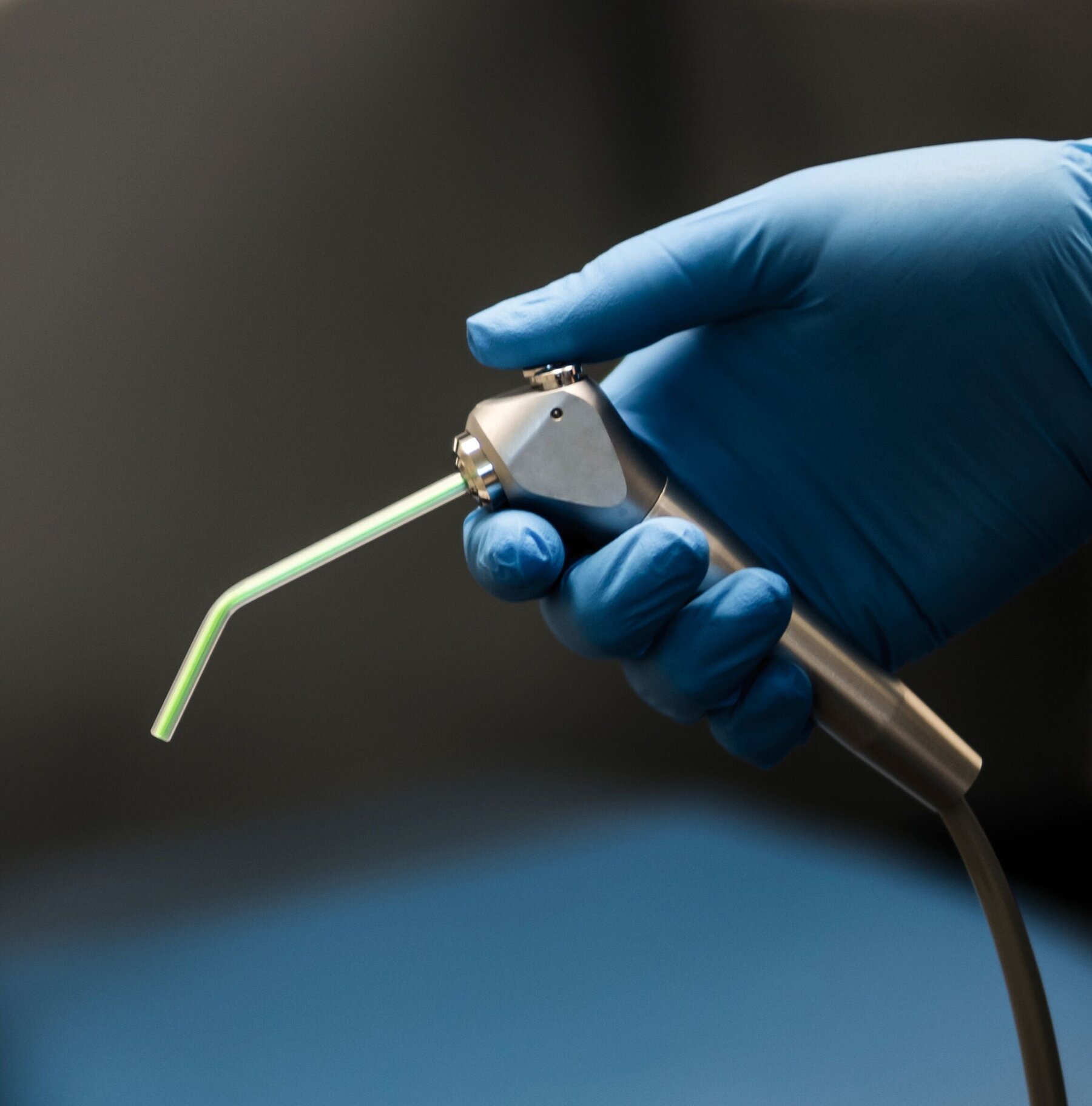 Hand in blue latex glove holding a dental air water syringe.