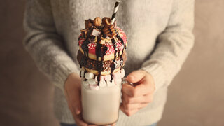 Mädchen hält Milchshake mit Donuts und anderen Süßigkeiten in einem Glas