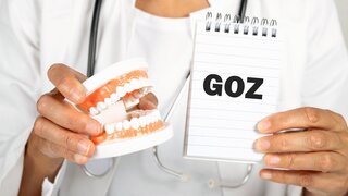 Eine Zahnärztin hält ein Modell eines Gebiss und einen Notizblock in der Hand auf dem GOZ steht