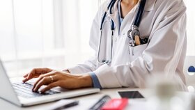Unrecognizable young female doctor working on laptop at the office desk.