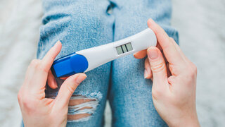 Frau schaut auf positiven Schwangerschaftstest