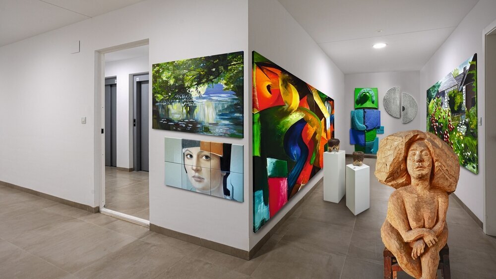 Long clean residential hallway featuring tiled flooring, white walls, recessed lighting, and elevator entrance in a contemporary apartment building.