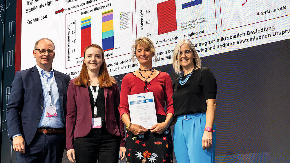 Der zweite Preis ging an Prof. Dr. Susanne Schulz (3. v. l., Universitätspoliklinik für Zahnerhaltungskunde und Parodontologie, Martin-Luther-Universität Halle-Wittenberg). Die ausgezeichnete Studie [2] untersuchte mikrobielle Zusammenhänge zwischen der subgingivalen Besiedlung und Karotis-Plaques. Die karotide Probeentnahme erfolgte intraoperativ im Rahmen von Karotis-Endarteriektomien. Die Analyse ergab, dass sich die Mikrobiota im Mundraum und in den Halsschlagadern unterscheiden. Taxa aus dem gingivalen Raum traten in Karotis-Plaques nur vereinzelt auf. Die Studie legt nahe, dass die vaskuläre Mikrobiota nicht ausschließlich oralen Ursprungs ist, sondern auch andere systemische Quellen hat.