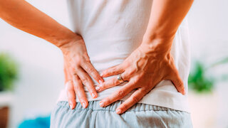 Frau hält sich mit den Händen den unteren Rückenbereich vor Schmerzen.