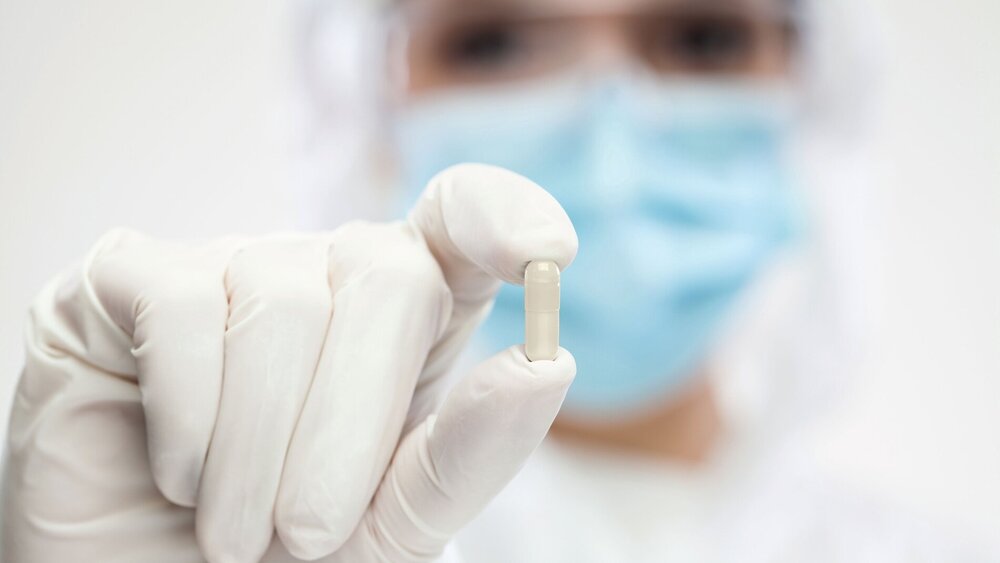 Female pharmacist wearing PPE personal protective equipment,coveralls,face mask,eyewear,gloves,holding green pill,selective focus,patient cure and remedy for illness disease,prescription drug concept