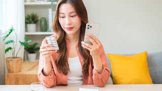 Patientin hält Tabletten in der Hand und sucht parallel Informationen auf dem Smartphone.