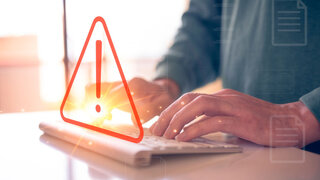 Mann tippt auf Tastatur mit dreieckigem Warnzeichen als Fehlermeldung durch Cyber-Angriff.