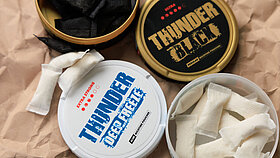Eine Sammlung von Snus und Nikotinbeuteln, aufgenommen auf einer braunen Papierunterlage in einer Wohnumgebung bei Tageslicht