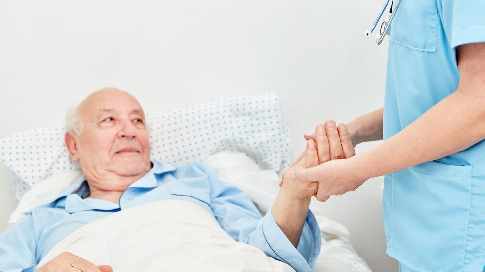 Kranker Senior liegt im Bett im Pflegeheim Kranker Senior liegt im Bett im Pflegeheim und wird betreut von einer Pflegehilfe
