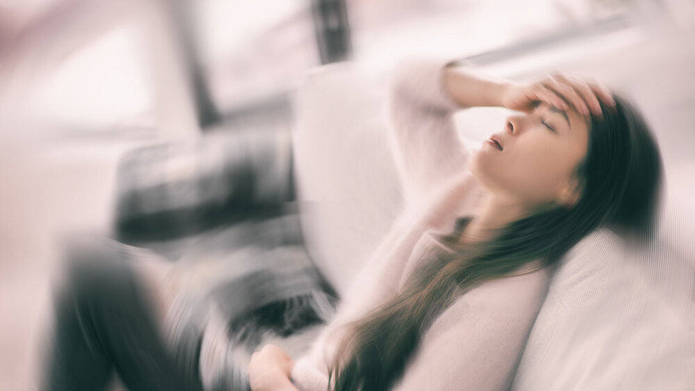 Sick woman with headache feeling faint vertigo holding head in pain with fever and migraine. Blurry motion blur background. Kranke Frau mit Kopfschmerzen