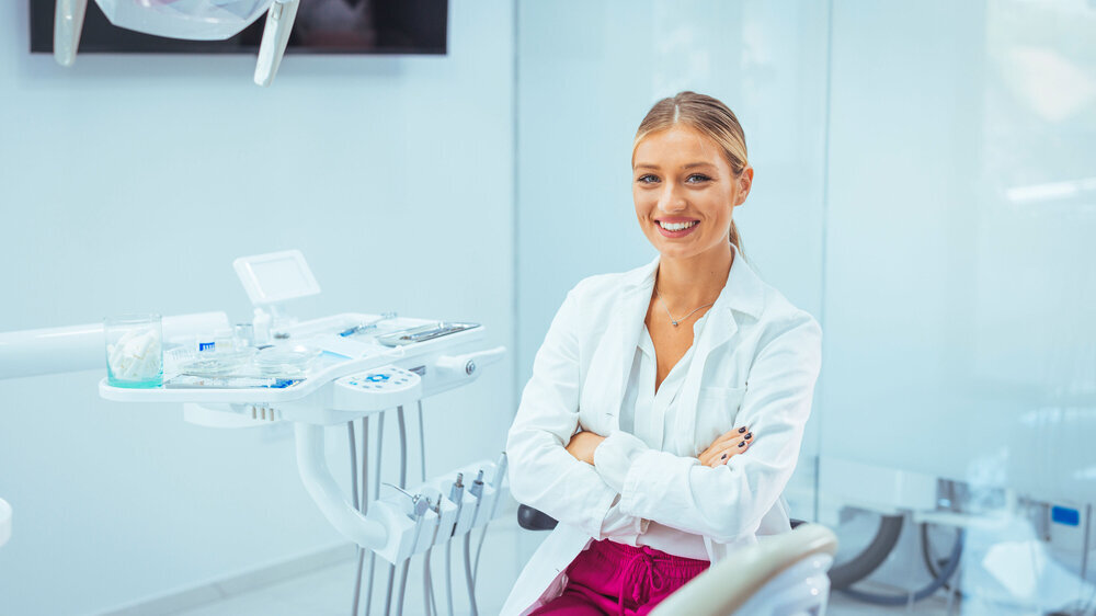 Portrait of a Caucasian woman dentist, sitting in her office next to a dentist chair, smiling. Portrait of female dentist. She standing at her office. Healthcare and medicine concept ZÄ