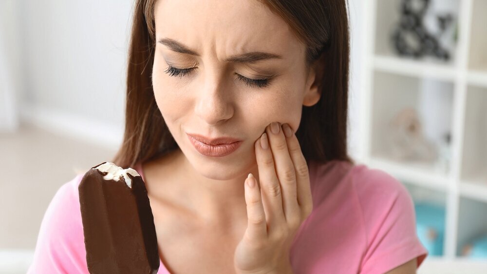 Young woman with sensitive teeth and cold ice-cream at home Zahnschmerzen, sensible Zähne