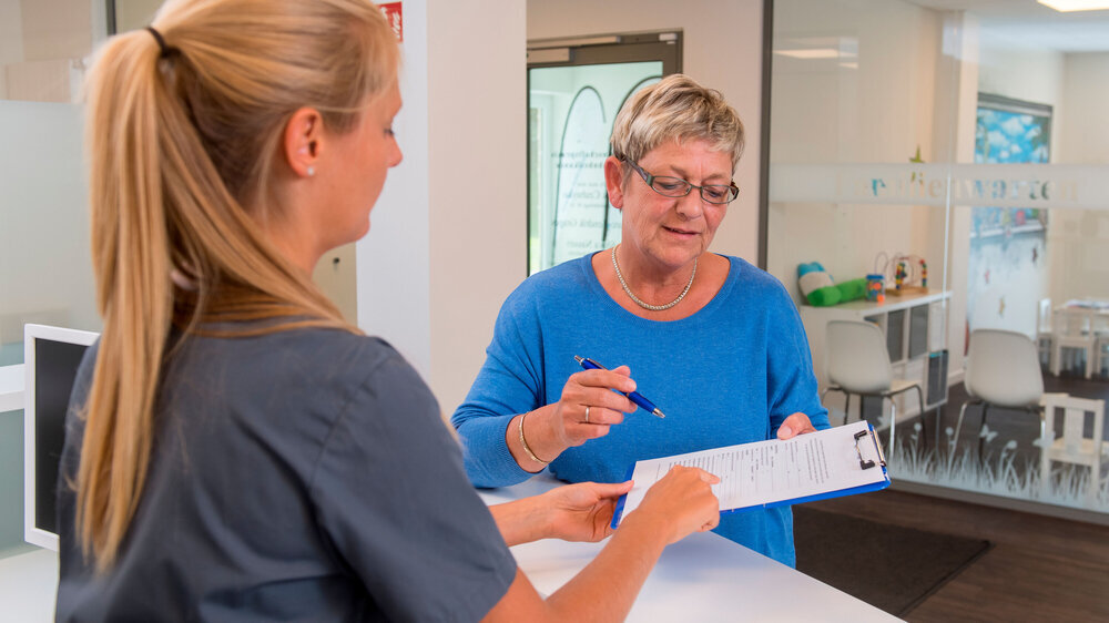 Eine medizinische Fachangestellte hilfe einer Patientin einen Fragebogen in der Arztpraxis auszufüllen.