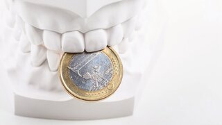 Umsatzsteuern Gebissabdruck mit Euromünze zwischen den Zähnen