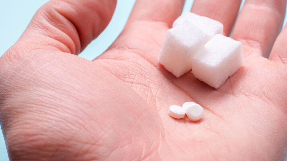 Choice of Sweetener in tablets or regular sugar. Alternative to sugar for diabetics. A man holds sugar and sugar substitute in his hand Zucker und Süßstoff