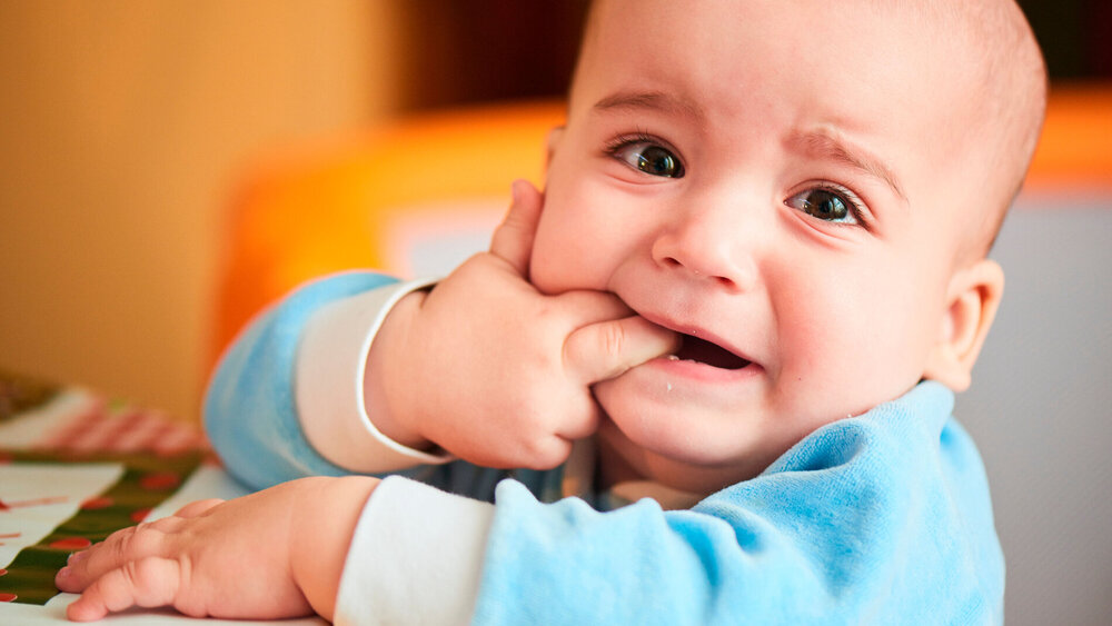 Baby weint, weil es zahnt und steckt sich Finger in den Mund.