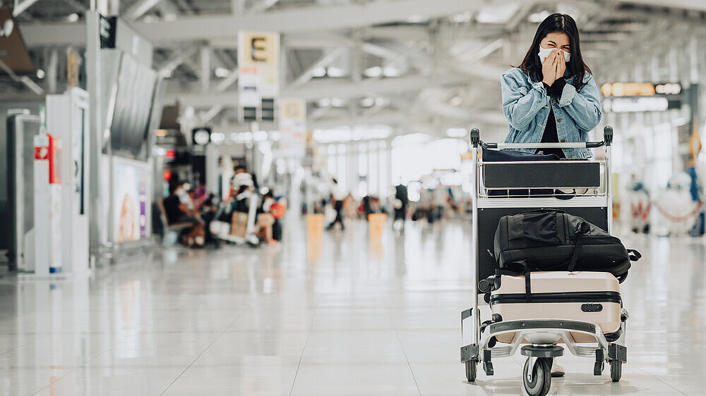 Asian woman traveler wearing mask sneezing Asian woman traveler wearing mask protect from coronavirus with luggage trolley sneezing