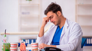 Junger Zahnarzt greift sich erschöpft an den Kopf, fühlt sich ausgebrannt.