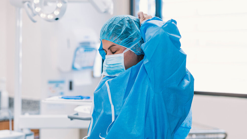 Zahnärztin legt sich Schutzkleidung an.