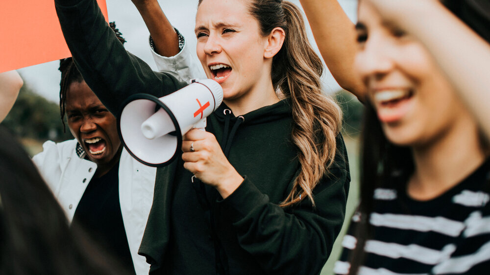Eine Gruppe von Aktivistinnen protestiert. Junge Frau mit Megafon im Vordergrund. Symbolbild Aktivistinnen. Junge Frau mit Megafon im Vordergrund.