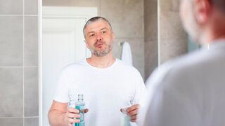 Mann benutzt Mundspüllösung vor einem Badezimmerspiegel.
