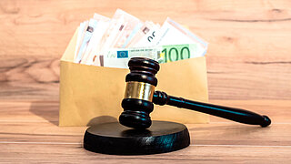 Ein Richterhammer vor einem Umschlag mit Euro-Banknoten.