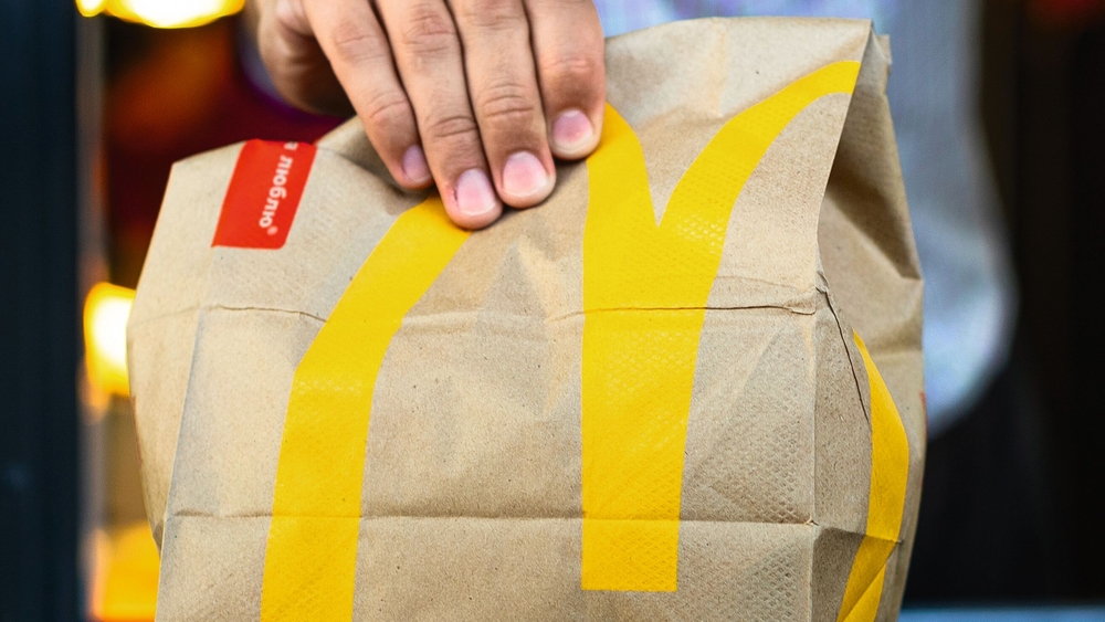 Sankt-Petersburg/Russia - July 21 2019: McDonald's worker holding bag of fast food. Hand with a paper bag through the window of mcdonalds car drive thru service. McDonald's