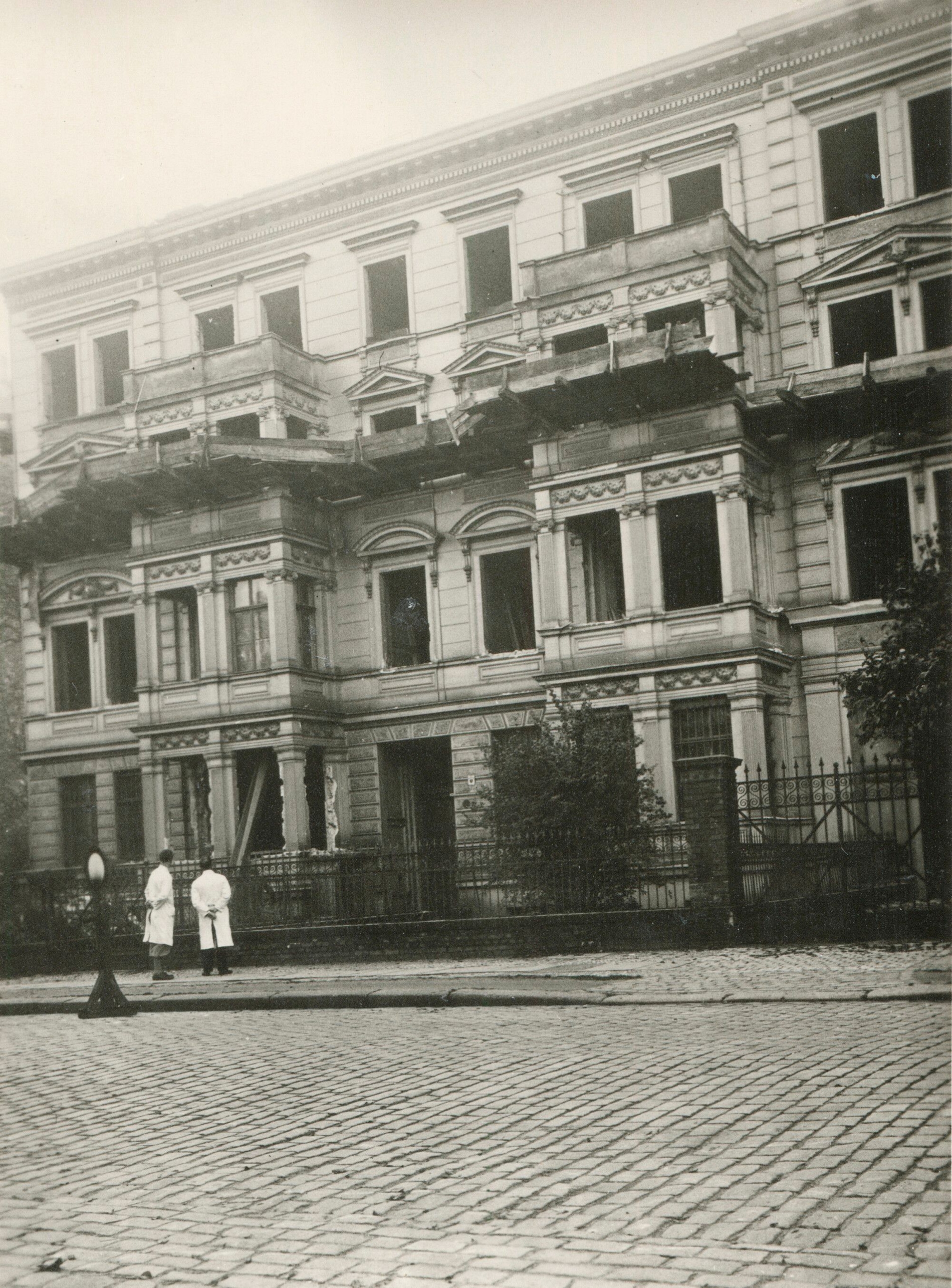 Zwei Foto: 2 Männer in weißen Arztkitteln betrachten das bereits entkernte Gebäude der ehemaligen Klinik von Dr. Karl Edel.